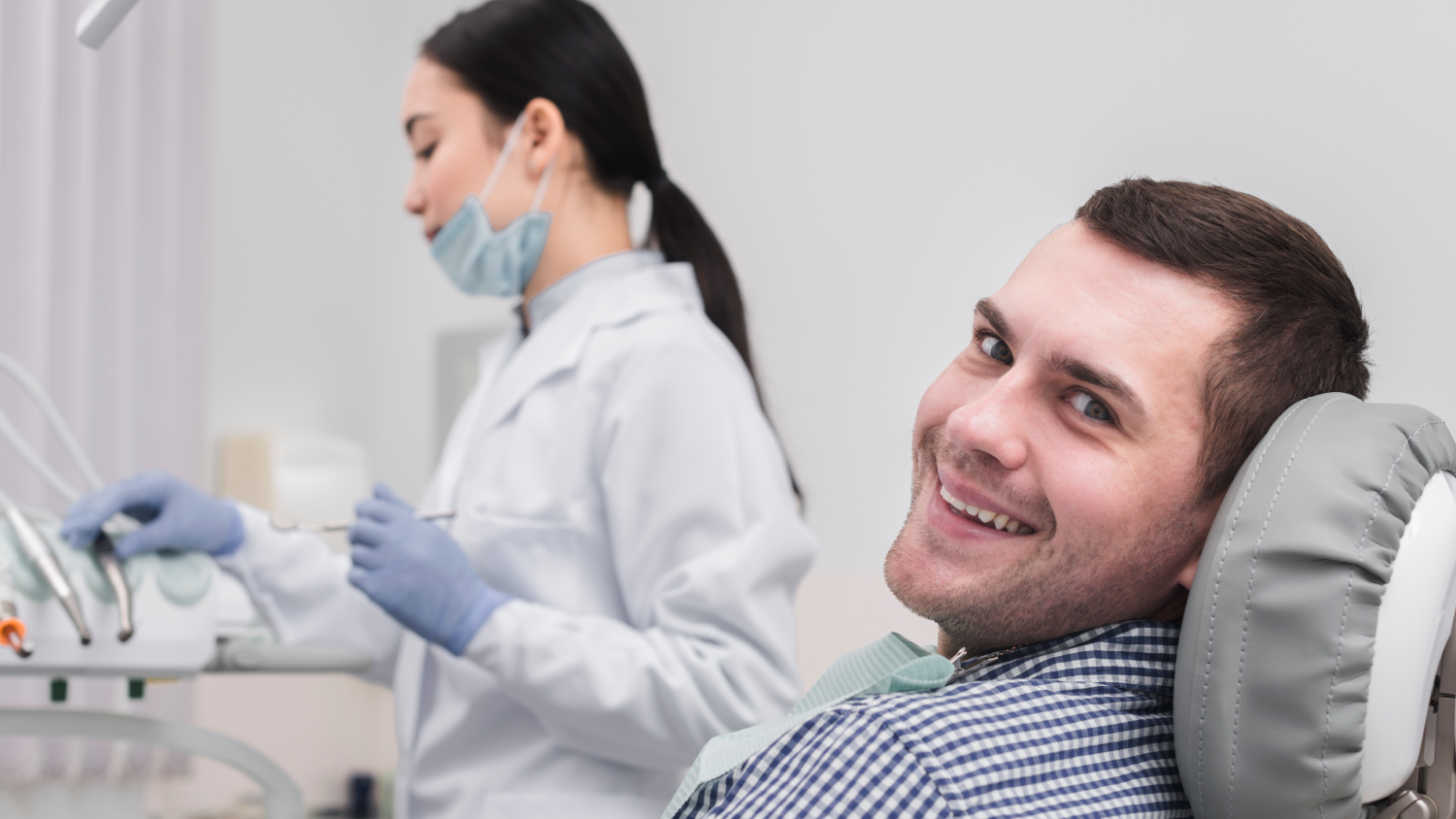 A dentist in a white coat holds a dental bridge while explaining the procedure to a smiling patient in a dental clinic
