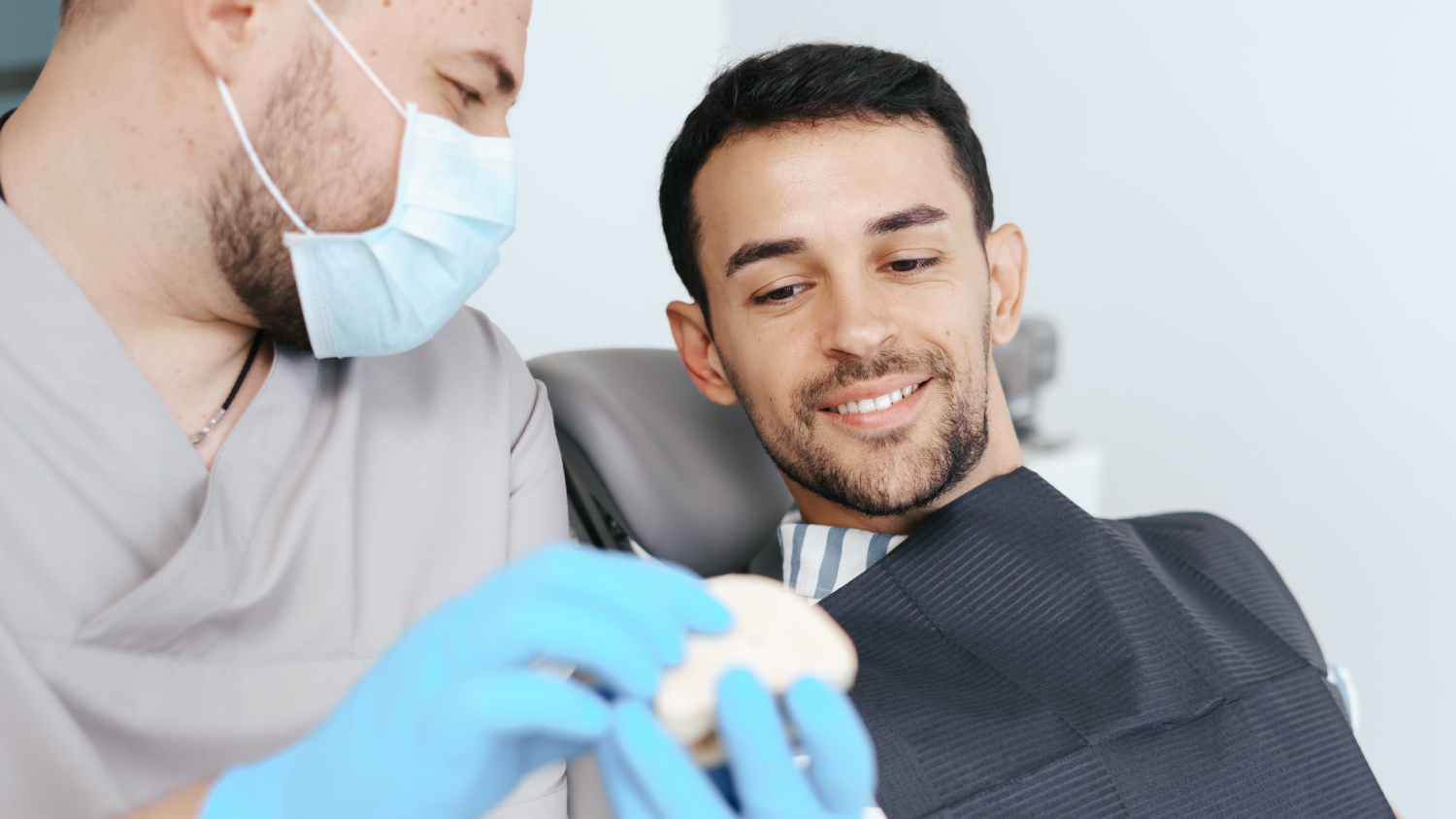 A compassionate Turkish dentist in a white coat gently examines a young adult patient's jaw and teeth in a sleek dental chair